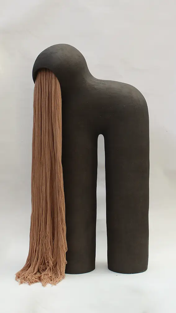 Sculpture Éruption #1 d'Elisa Uberti en grès noir, silhouette à deux jambes arquées. Une longue frange de laine retombant de l'ouverture comme une bouche