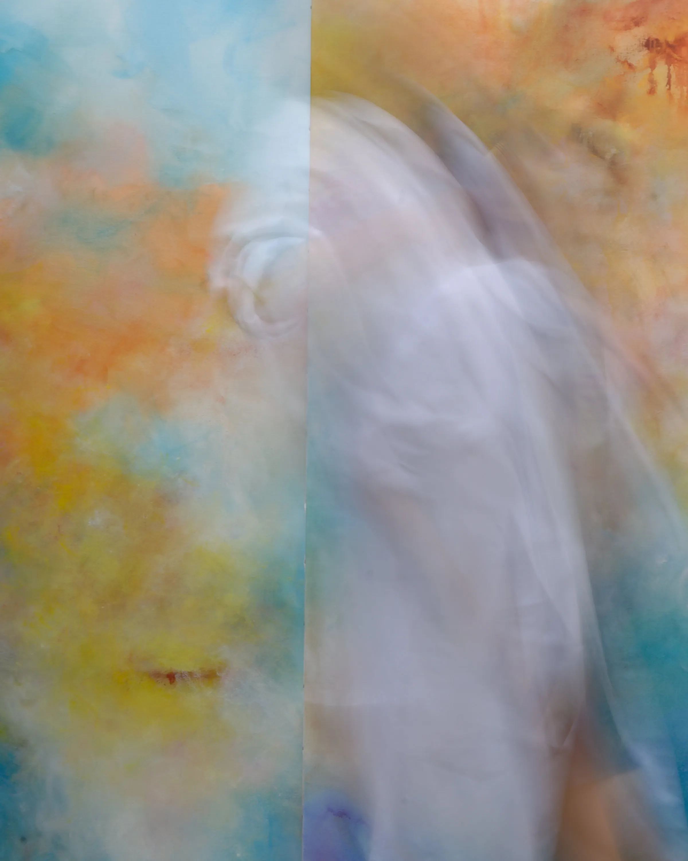 Silhouette floue de l'artiste peintre Mai Khanh Pham To, en blouse de peintre blanche, manches retroussées, de trois-quart dos, un pinceau à la main. Elle est devant une très grande toile colorée dans les tons d'orange, bleus et rosés.